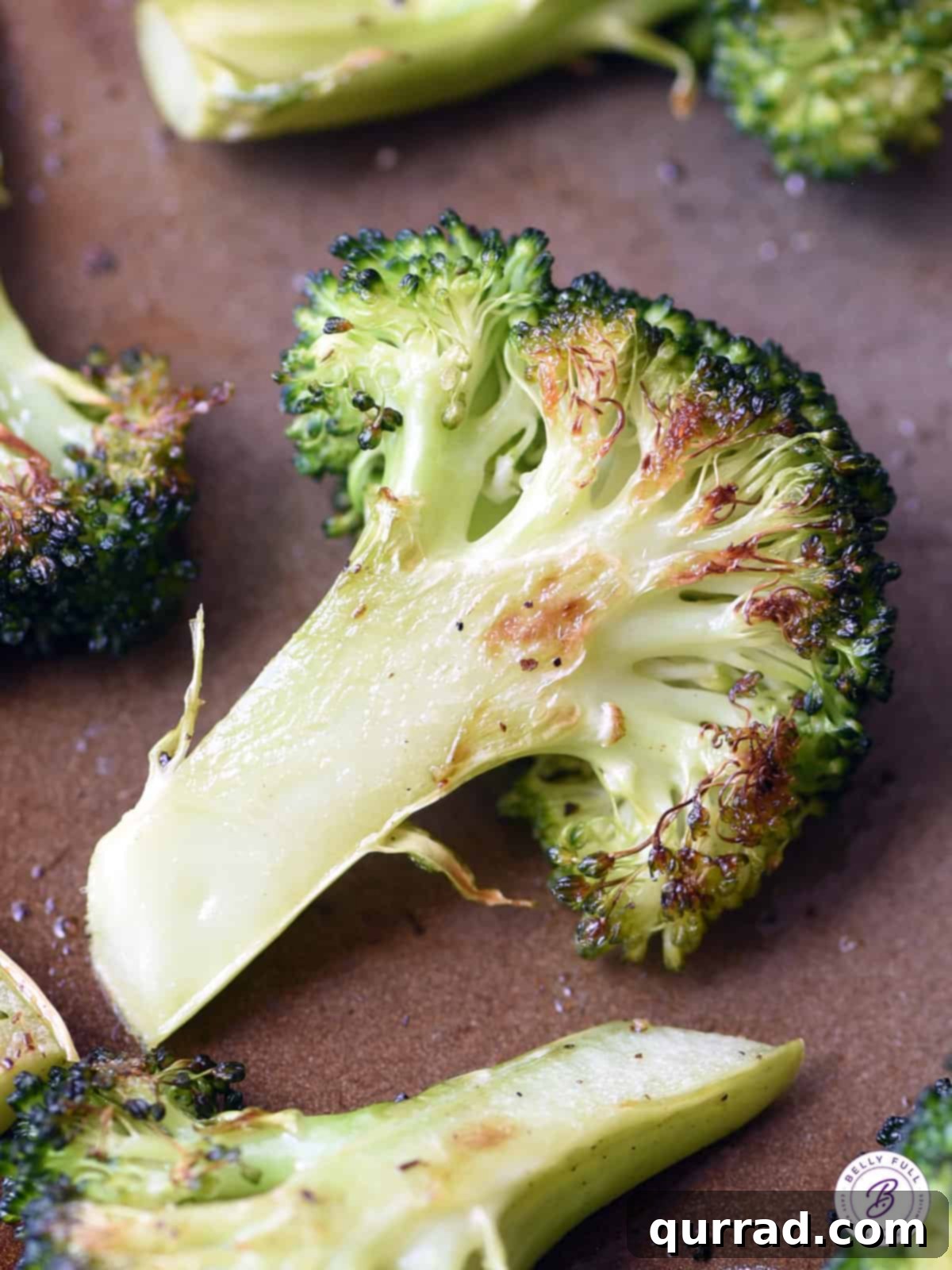Crispy Roasted Broccoli 4 Close-up of a perfectly roasted broccoli floret on a baking sheet, showing crispy edges and tender center, adorned with tiny browned bits.