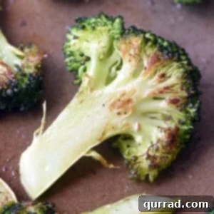 Crispy Roasted Broccoli 5 Crispy roasted broccoli florets on a baking sheet, golden brown with slight charring.
