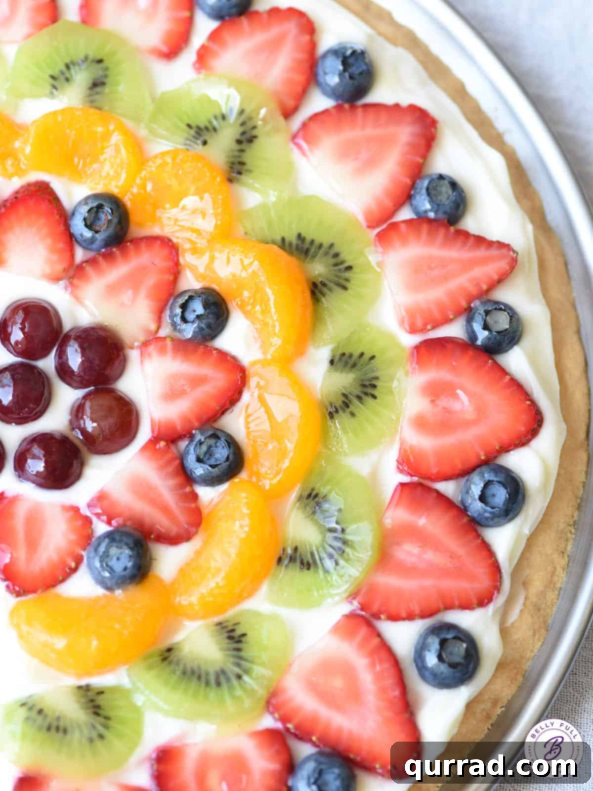 Vibrant Fruit Pizza 2 A beautifully arranged Dessert Fruit Pizza with a sugar cookie crust, topped with cream cheese frosting, and a variety of fresh, colorful fruits, all glistening with a citrus glaze.