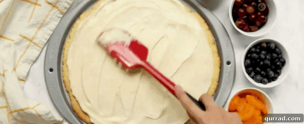Vibrant Fruit Pizza 8 Spreading the creamy cream cheese topping over the cooled sugar cookie crust.