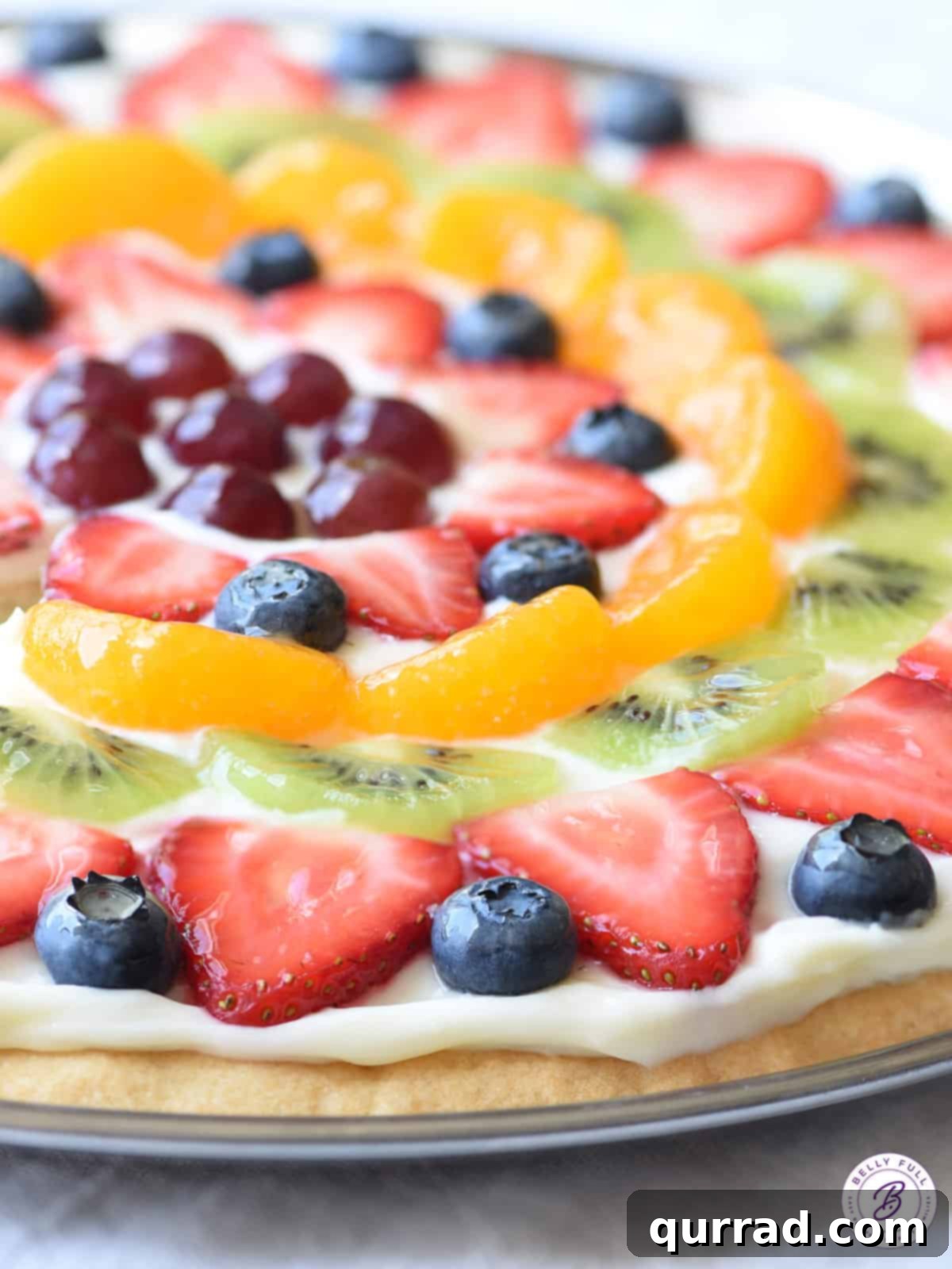 Vibrant Fruit Pizza 11 A large, glazed, and colorful sliced fruit pizza, topped with an array of fresh berries, kiwi, and mandarin oranges.