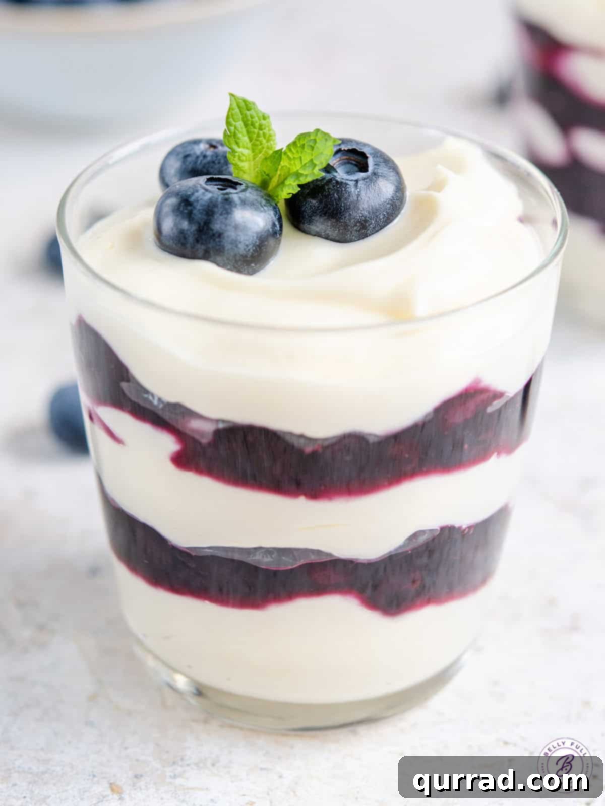 Close-up of a blueberry cheesecake parfait in a glass jar, showing distinct layers of creamy white cheesecake filling and dark purple blueberry sauce.