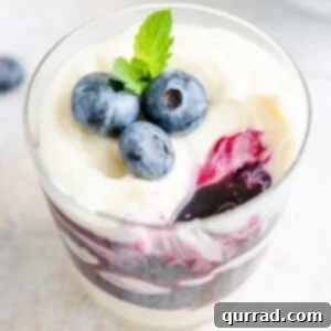 A top-down view of a blueberry cheesecake parfait with fresh blueberries and a small wooden spoon, ready to be enjoyed.