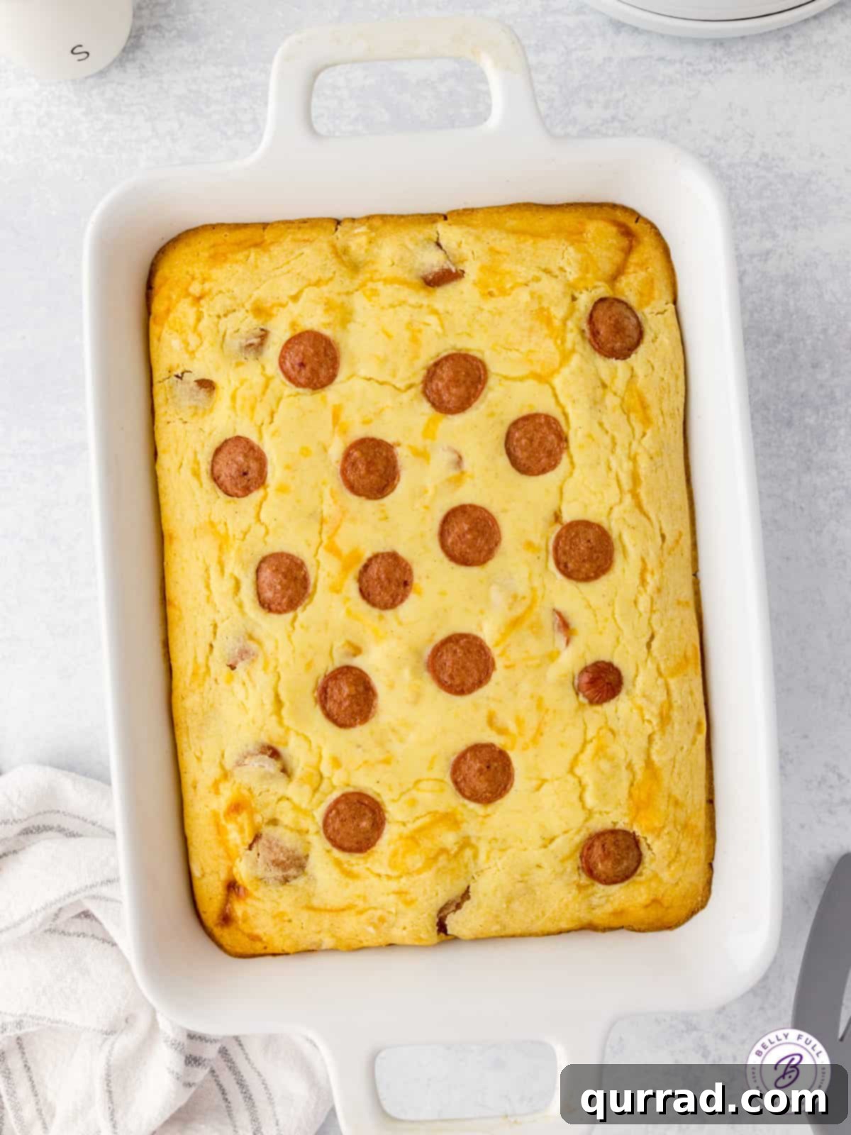 An overhead view of an uncut Corn Dog Casserole in a baking dish, revealing the arrangement of hot dog pieces within the golden cornbread topping.