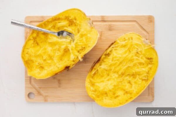 2 roasted spaghetti squash halves with pulled strands on cutting board
