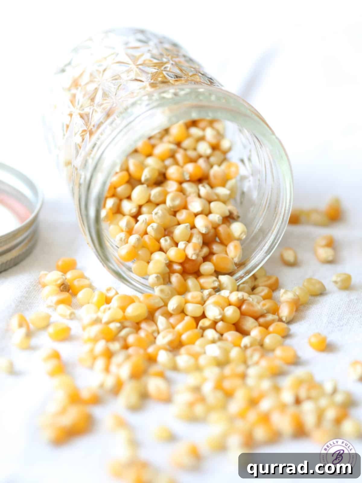 Movie Night Magic 4 Popcorn kernels spilling out of a glass jar onto a wooden surface, highlighting the raw ingredient.