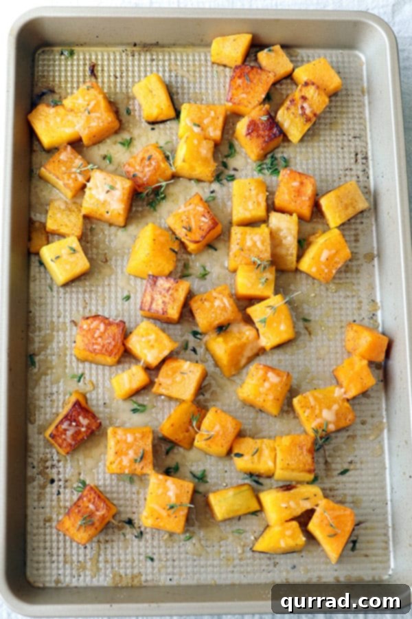 Roasted Butternut Squash on Baking Sheet Perfectly roasted butternut squash cubes, golden and tender, scattered on a baking sheet with herbs.