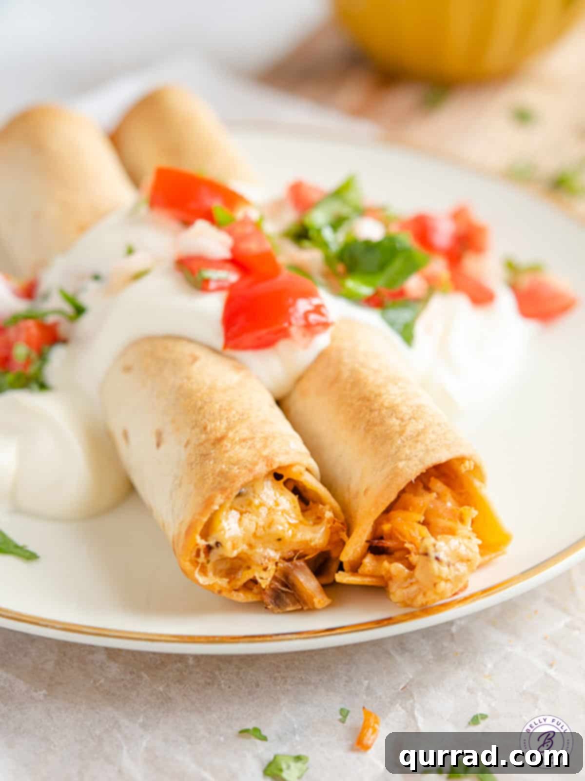 Crispy Pulled Pork Taquitos 5 Two baked pulled pork taquitos on a white plate, garnished with fresh cilantro and a lime wedge.
