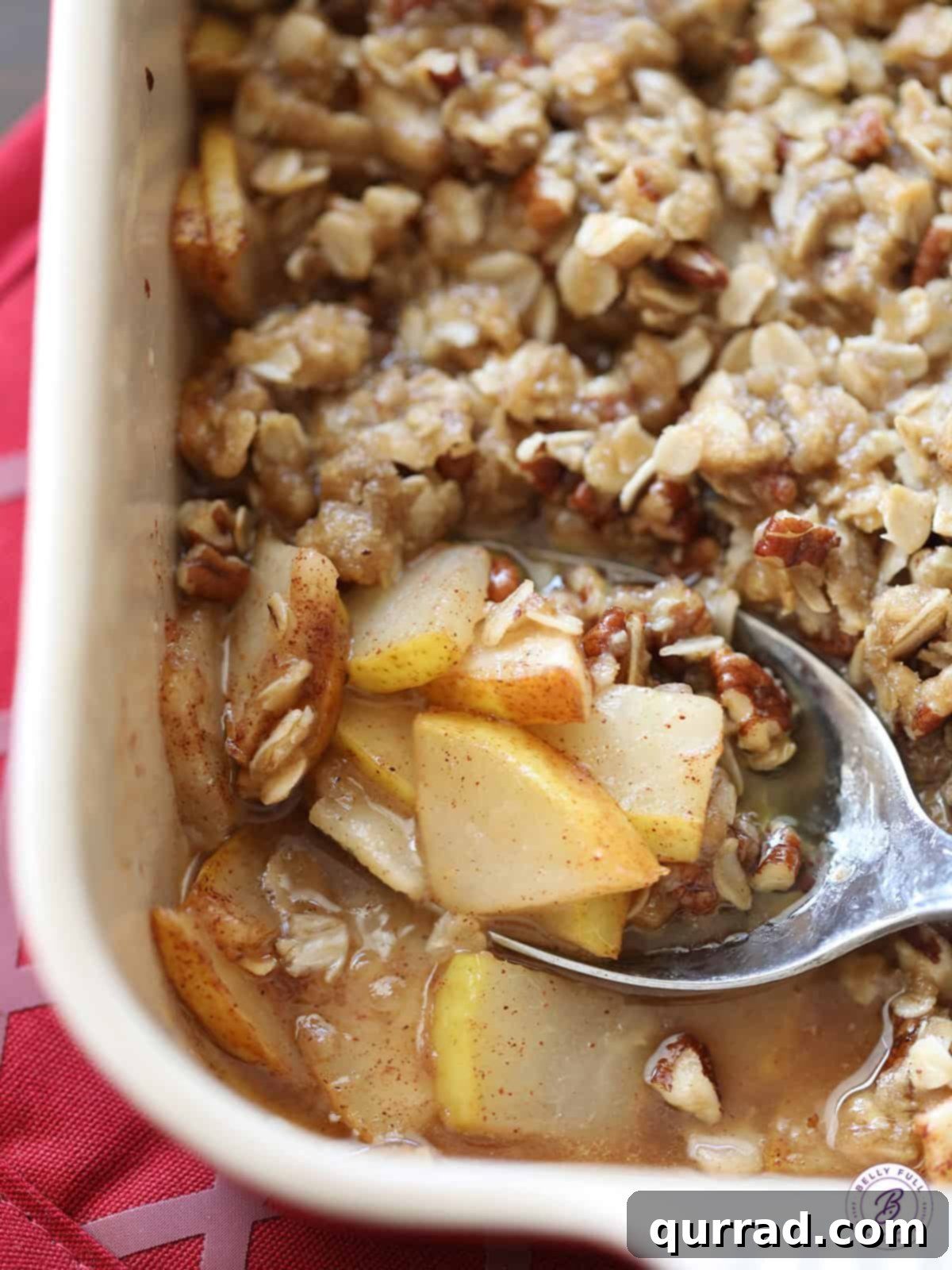 Close up of a golden-brown pear crisp in a white baking dish, showing the crunchy topping and tender fruit beneath.