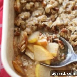 Pear crisp in a white baking dish with a spoon, ready to be served.