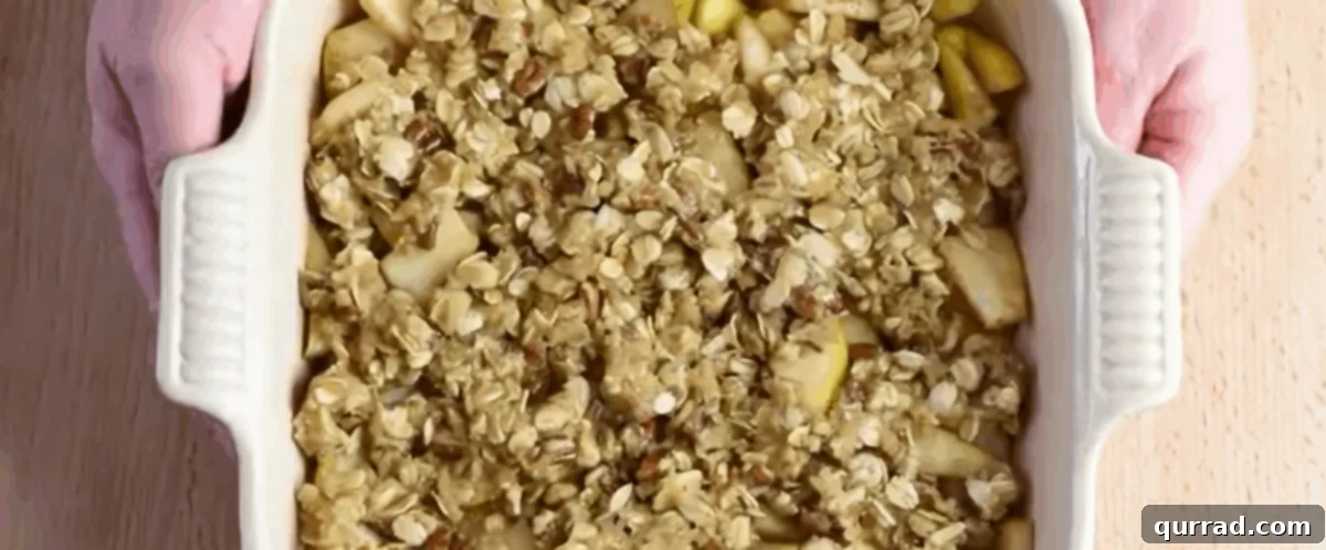 The pecan-oat topping evenly sprinkled over the pear filling in a white baking dish, ready for baking.