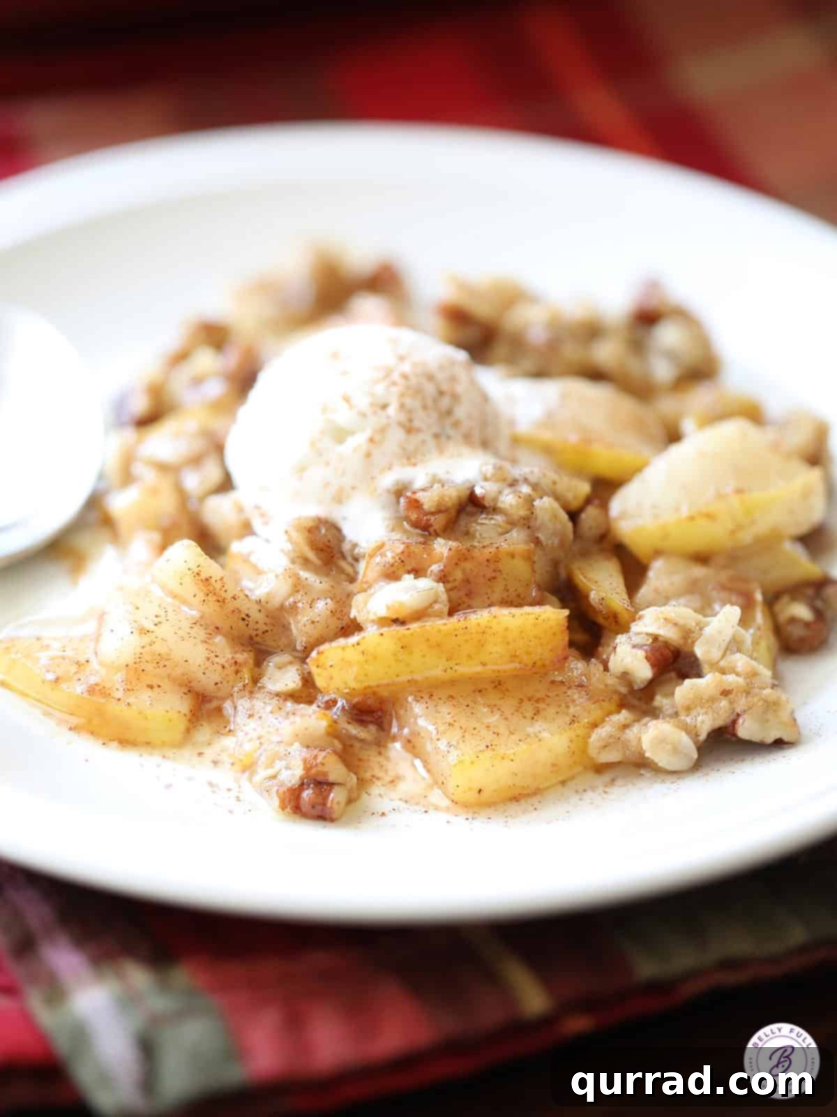 A serving of warm pear crisp with oat topping and a scoop of melting vanilla ice cream on a white plate.