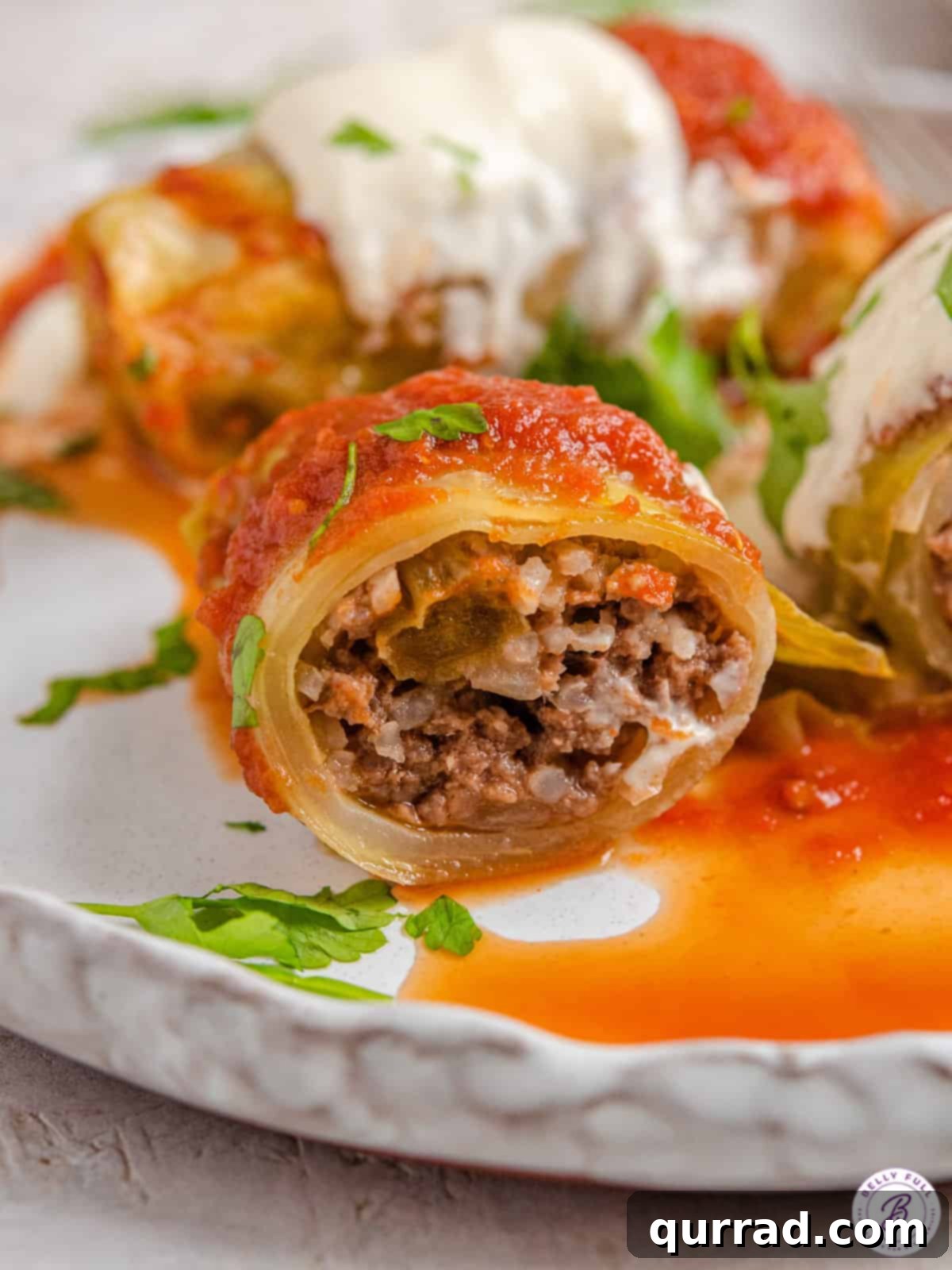 Savoring Stuffed Cabbage Rolls: Inside View of Comfort Food A close-up view of a perfectly cooked stuffed cabbage roll, sliced neatly in half to reveal its tender beef and rice filling, resting on a white plate with a generous pool of rich tomato sauce.
