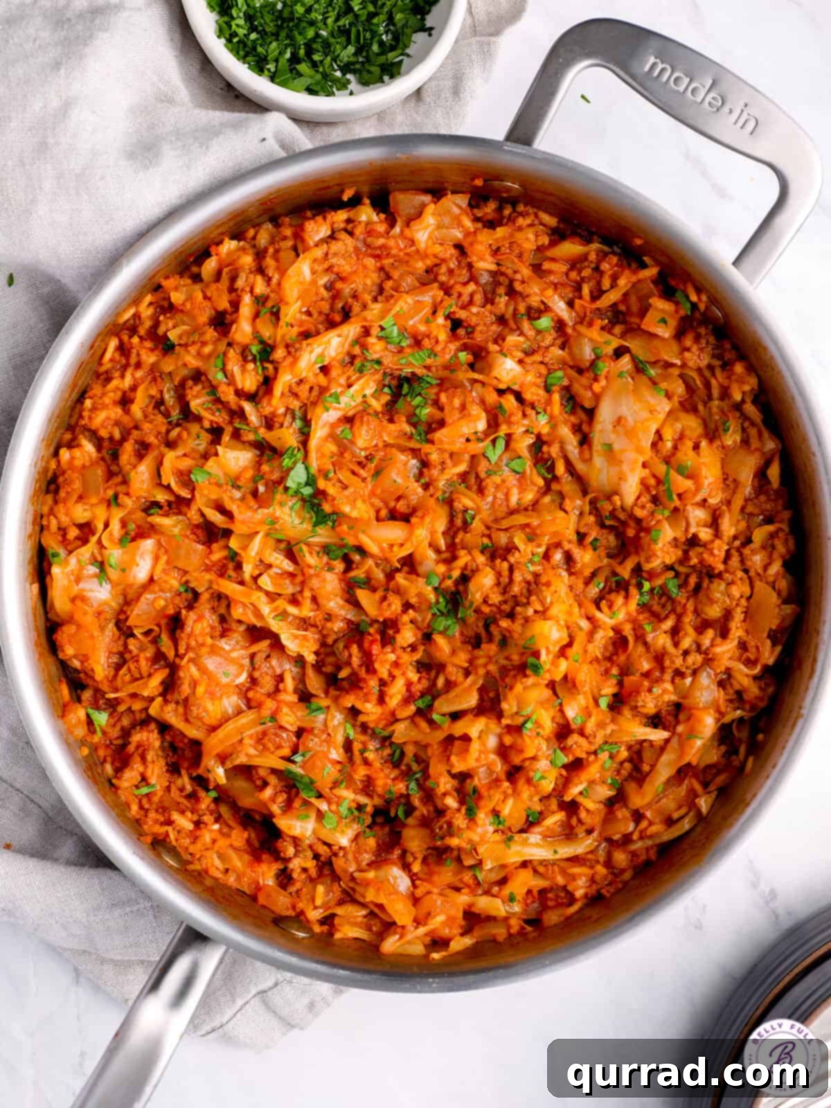 Lazy Cabbage Casserole 3 A large skillet filled with cooked unstuffed cabbage rolls, featuring tender cabbage, ground beef, and rice, garnished with vibrant chopped parsley.