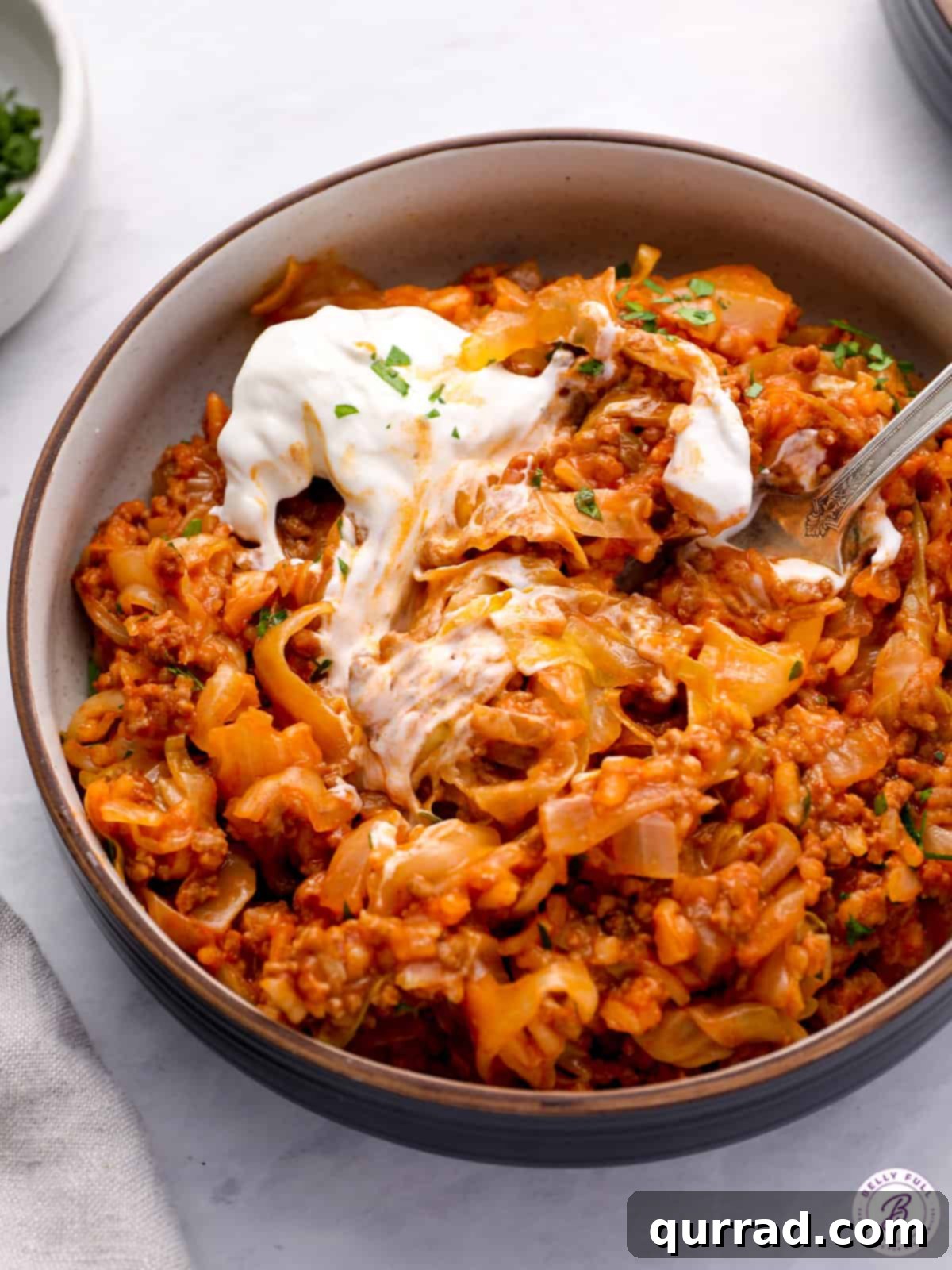 Lazy Cabbage Casserole 5 A serving of unstuffed cabbage rolls in a rustic bowl, topped with sour cream and a sprig of fresh parsley, with a fork poised to scoop a bite.