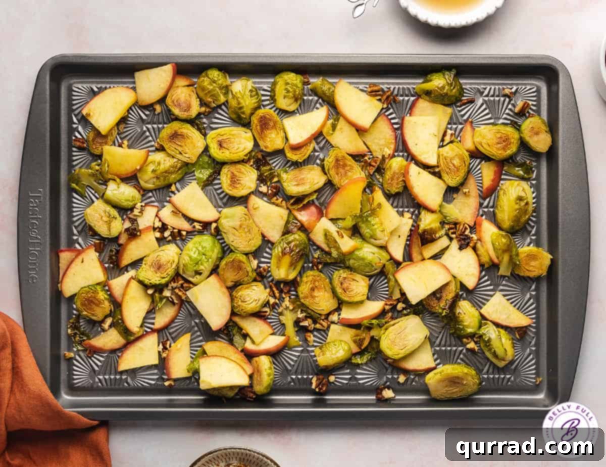 Sweet & Savory Roasted Brussels with Apples 3 Roasted brussels sprouts and apples spread on a baking sheet, half-cooked.