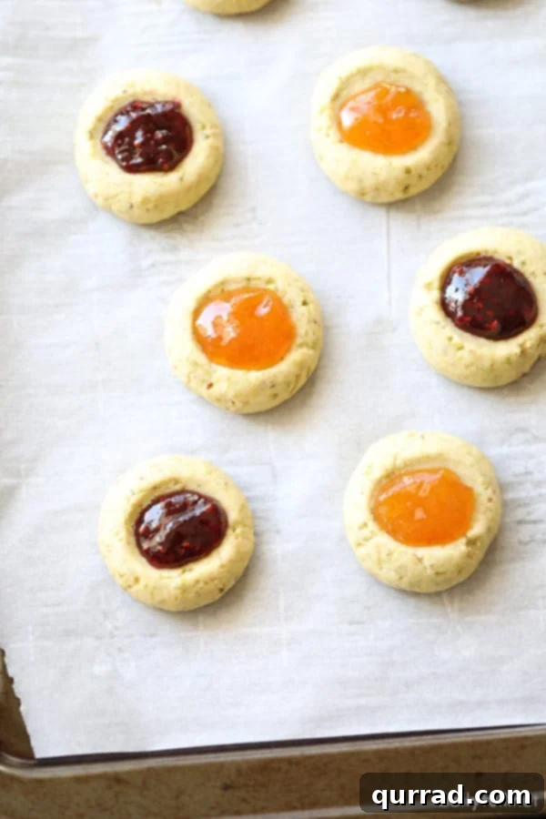 These Thumbprint Cookies are buttery shortbread, filled with your favorite jam and topped with powdered sugar. Perfect for the holidays or anytime! thumbprint cookies filled with jam on baking sheet