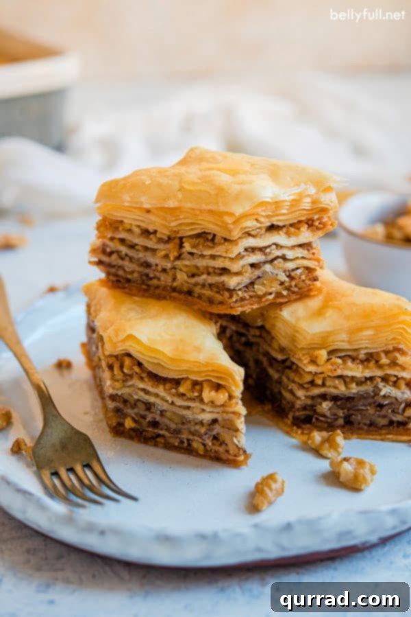 Delicious individual Baklava servings, perfect for dessert. Three individual pieces of golden Baklava, neatly stacked on a white plate, showing the flaky layers and nut filling.