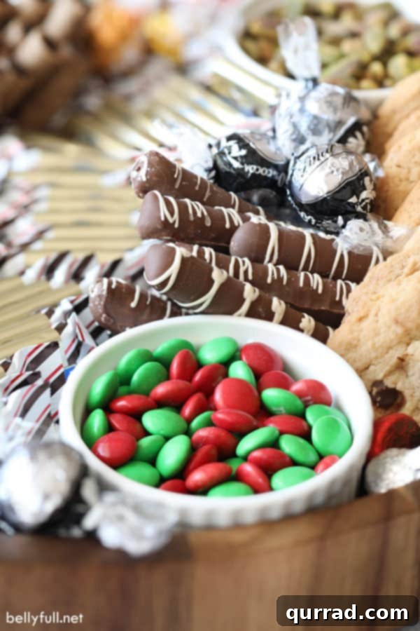 A beautiful Christmas Charcuterie Board featuring red and green M&Ms, a variety of truffles, festive cookies, and delicious chocolate-covered pretzels