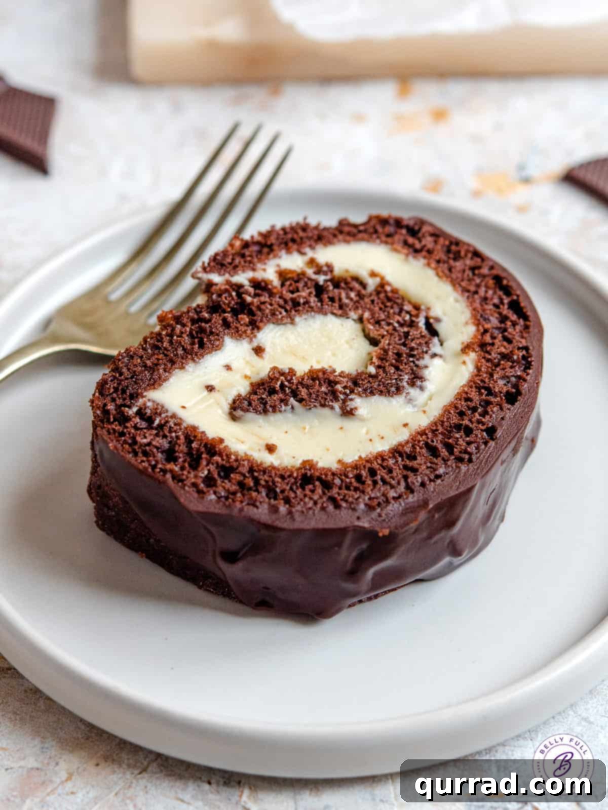 This easy Chocolate Swiss Roll Cake has a light sponge, creamy filling, and coated with a silky ganache. A slice of chocolate Swiss roll cake a on plate.