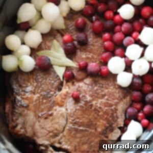 Chuck roast, cranberries, and pearl onions arranged in a slow cooker before cooking begins