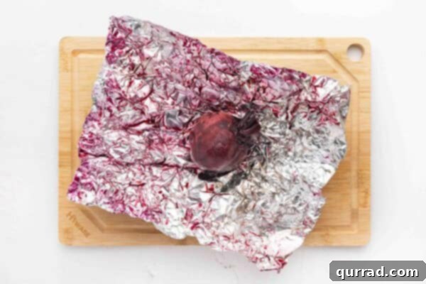 a whole roasted beet, still in its foil, being checked for tenderness with a skewer