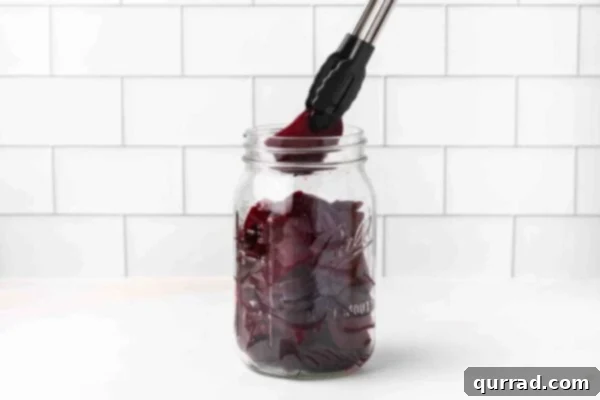Sliced beets being transferred into a glass jar with tongs