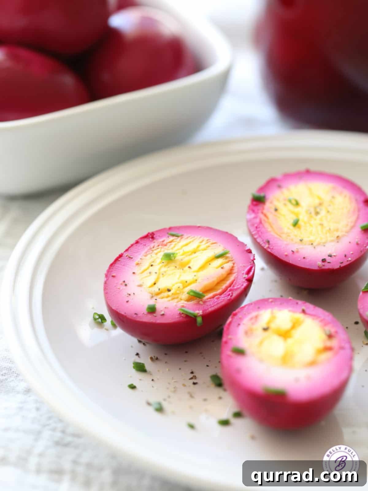 Ruby Red Pickled Eggs 4 beet pickled egg halves on white plate garnished with chives and pepper