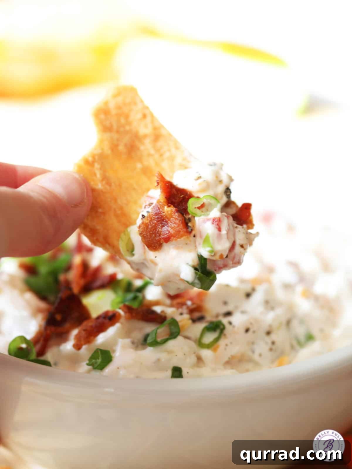 Loaded BLT Dip 4 Close-up shot of a generous scoop of creamy BLT dip perfectly perched on a crunchy pita chip, showcasing its rich texture and colorful ingredients.