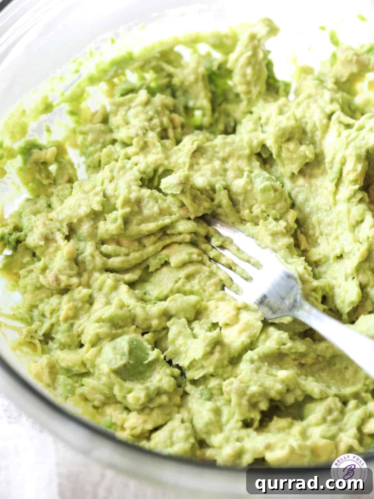 Close-up of a fork mashing ripe avocado in a bowl, showcasing the creamy texture before other ingredients are added.