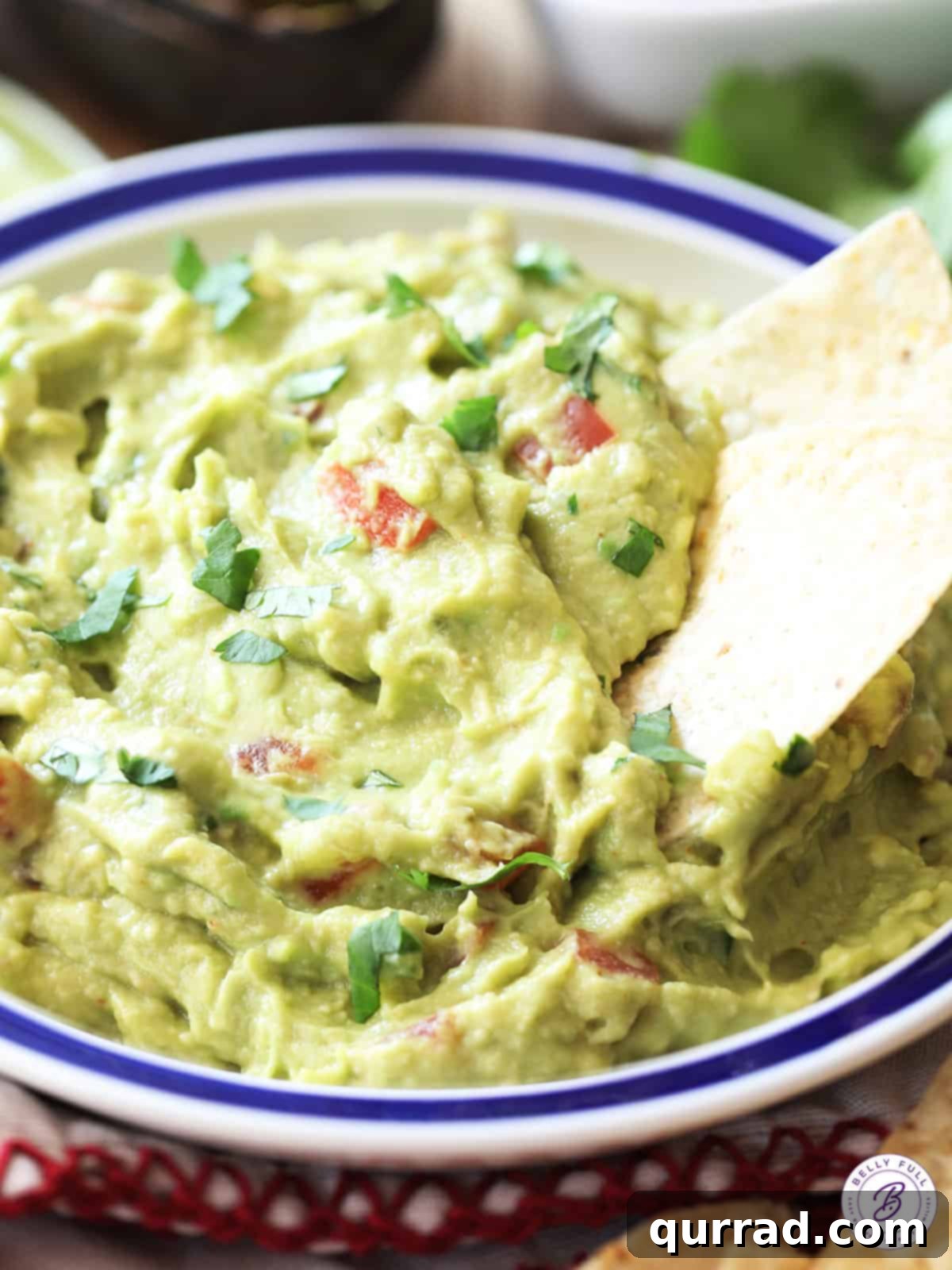 A tortilla chip being dipped into a bowl of creamy, fresh guacamole, ready to be enjoyed.