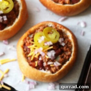 Mini bread bowls filled with chili, topped with cheese and other garnishes.