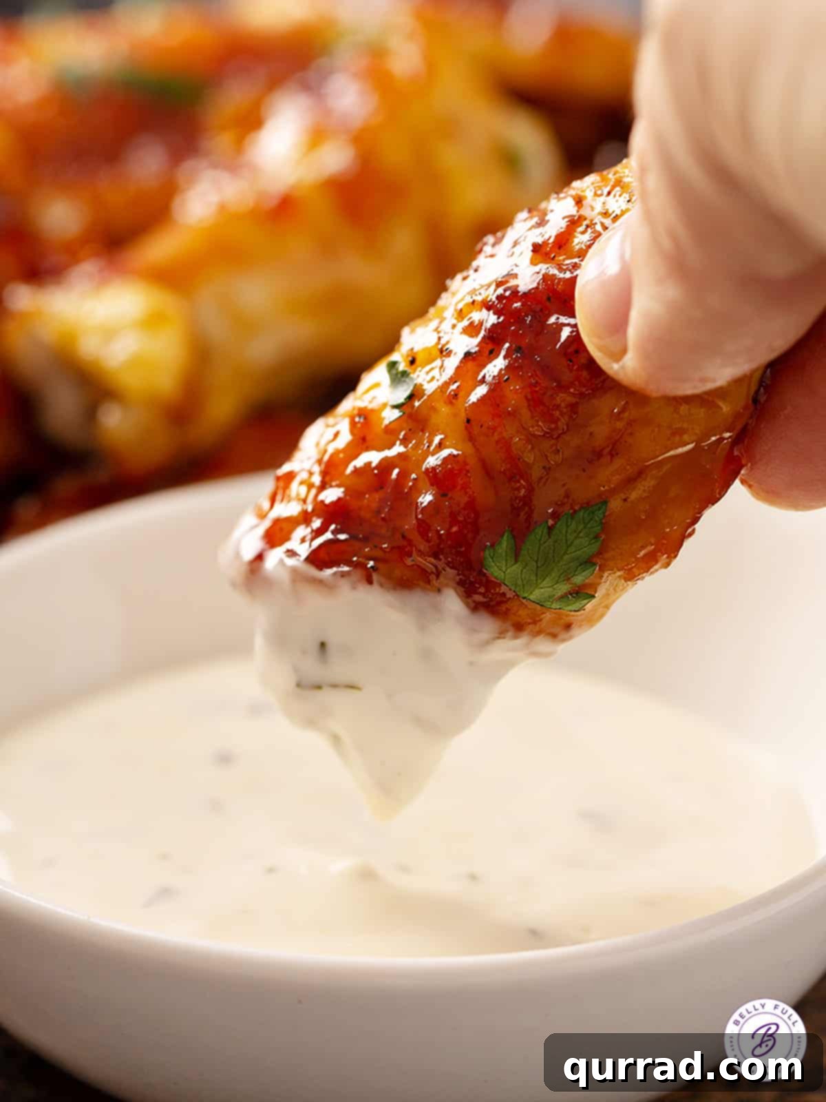 Glazed baked chicken wing being dipped into a bowl of creamy tzatziki sauce