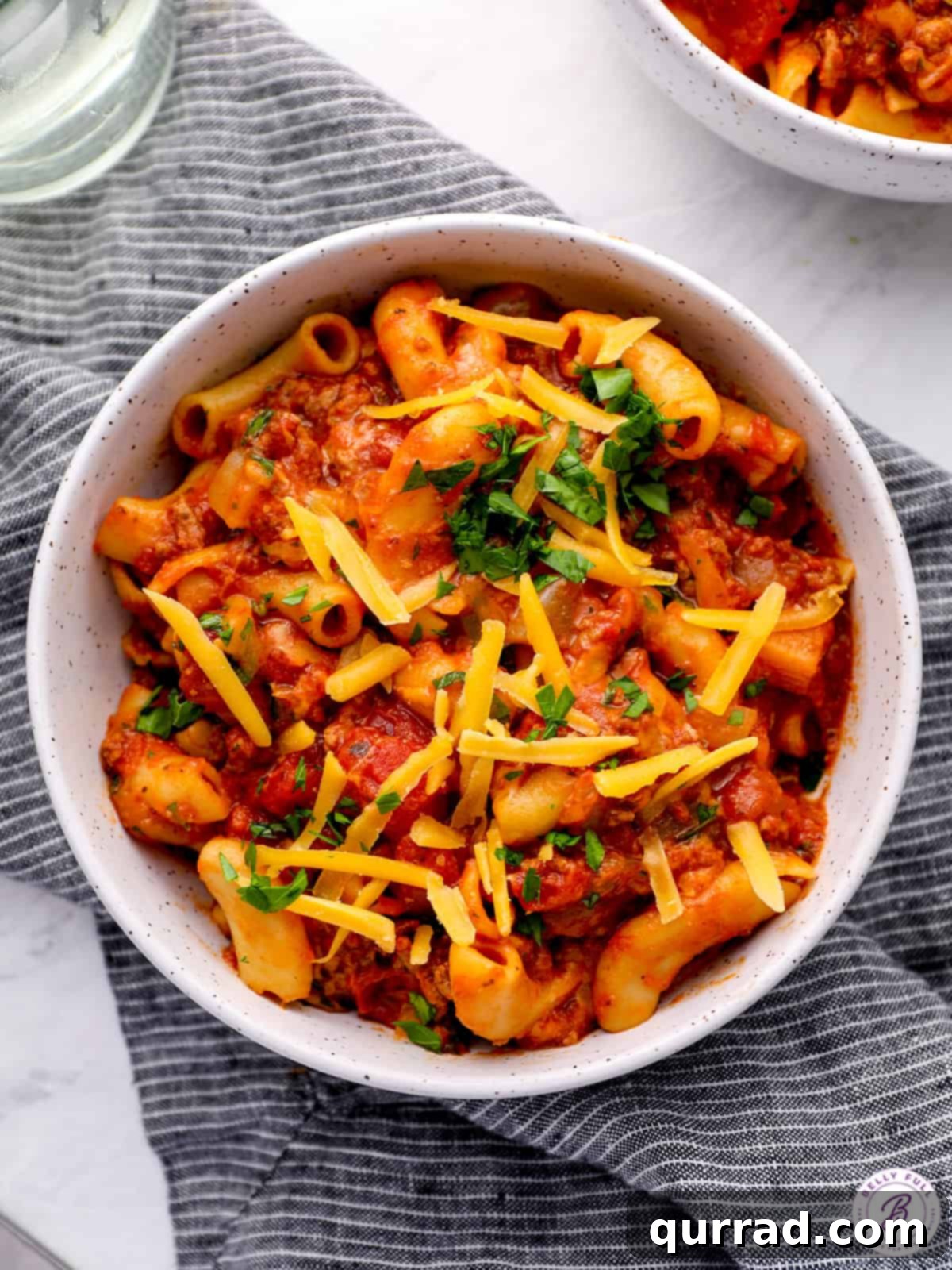 Hearty Weeknight American Goulash 2 A comforting bowl of American Goulash, featuring a rich blend of tomato sauce, seasoned ground beef, and macaroni pasta, topped with melted shredded cheddar cheese.