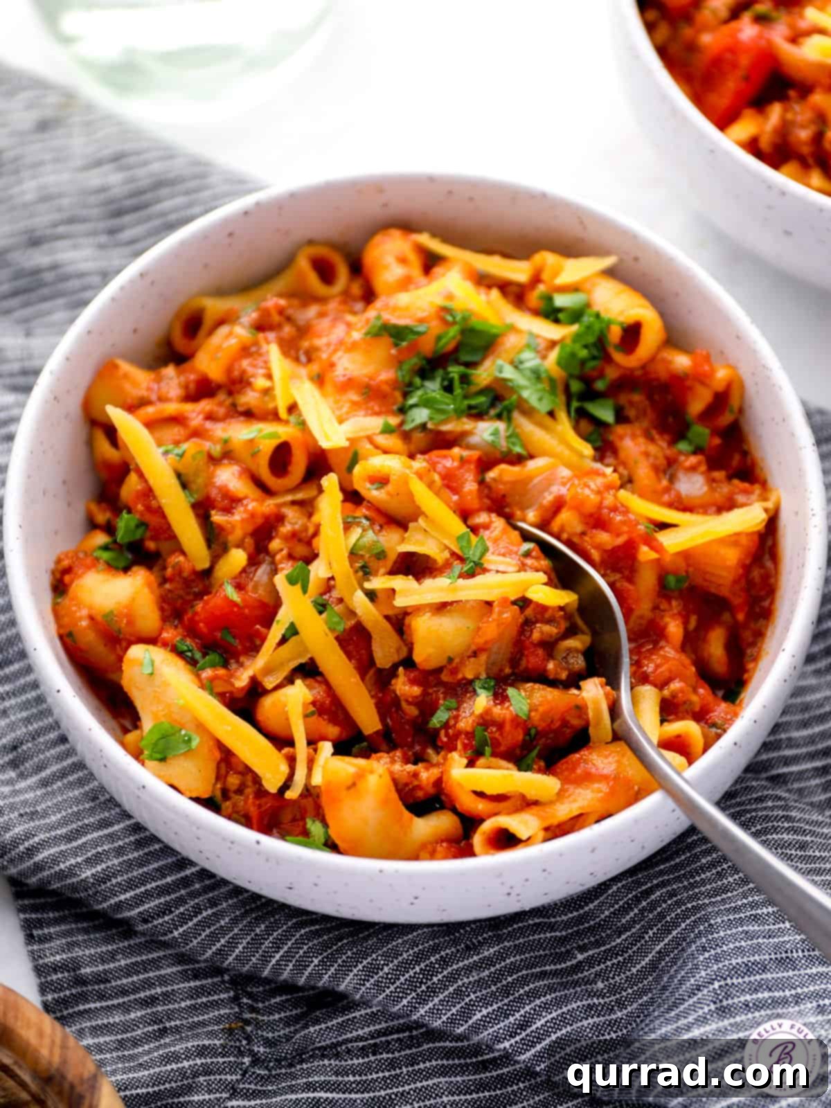 Hearty Weeknight American Goulash 5 A close-up shot of a bowl of cooked beef and macaroni goulash, with a spoon resting in the hearty, cheesy dish, inviting you to take a bite.