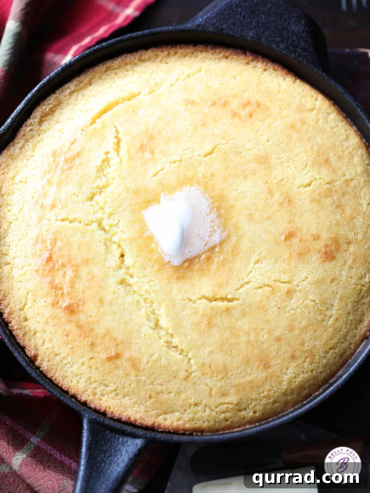 Golden Hearth Cornbread 2 Overhead view of homemade cast iron skillet cornbread with a pat of melted butter, ready to serve.