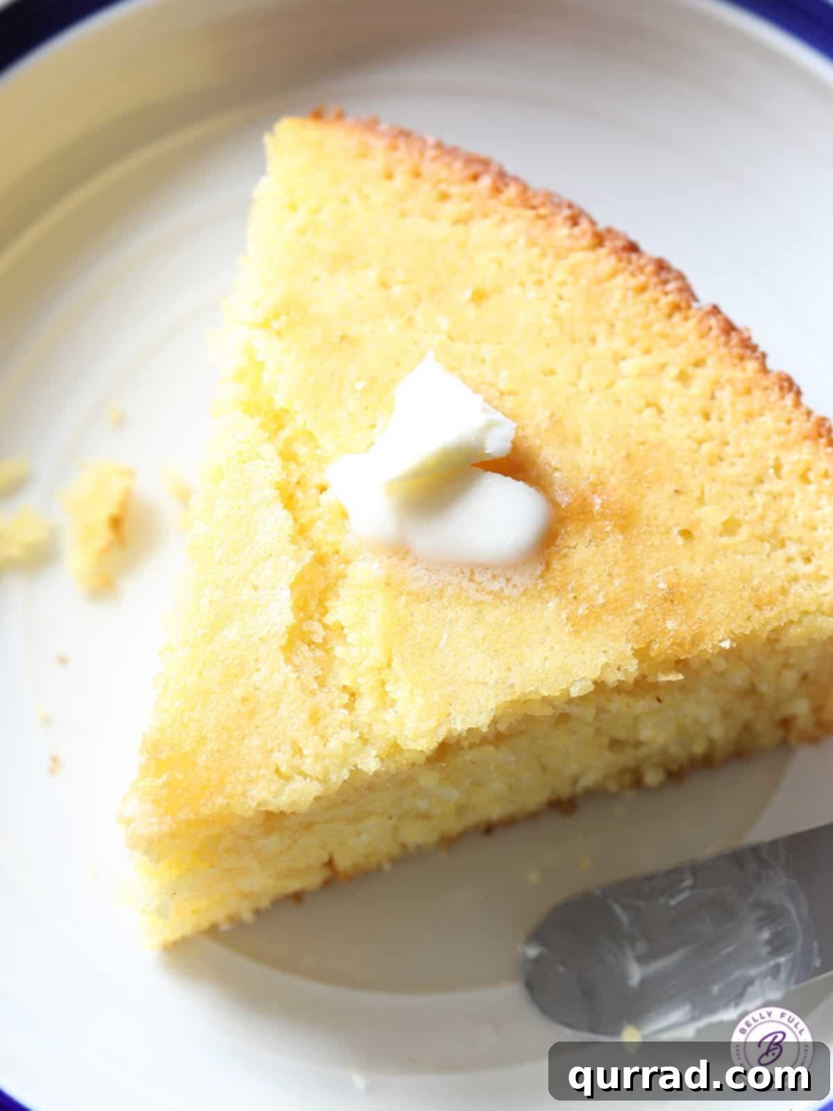 Golden Hearth Cornbread 4 A wedge of golden cornbread on a white plate with a butter knife beside it, showcasing its fluffy texture.