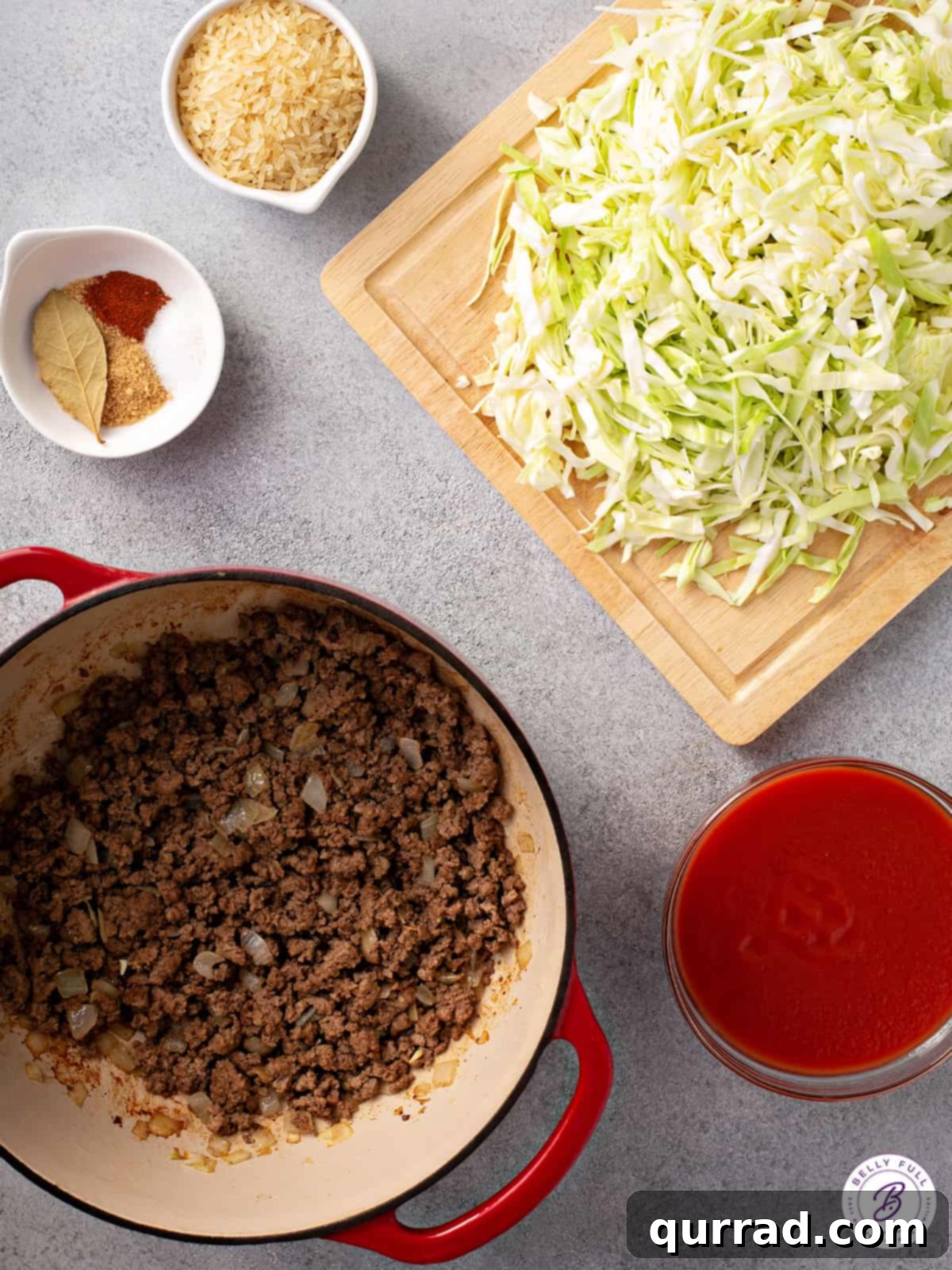 Deconstructed Cabbage Rolls 4 Organized ingredients for cabbage roll soup on a wooden surface: olive oil, ground beef, onion, garlic, cabbage, beef broth, tomato sauce, rice, brown sugar, Worcestershire sauce, and various spices.