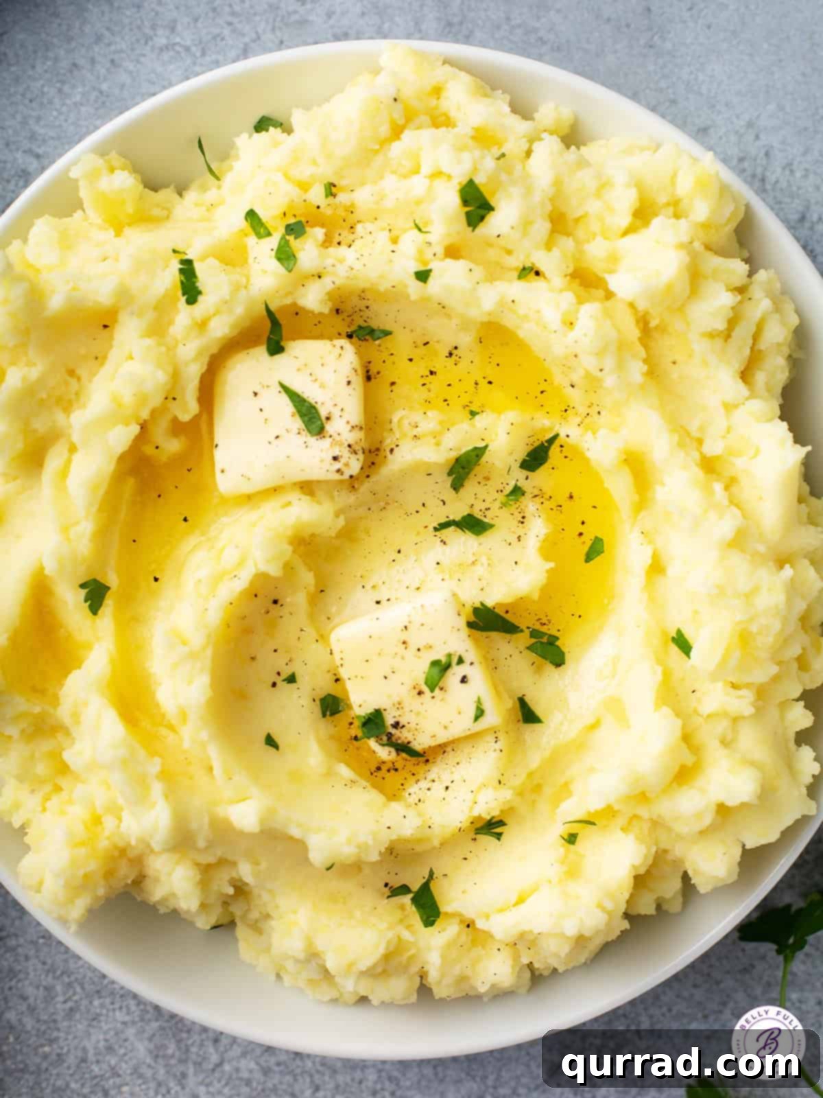 Melt-in-Your-Mouth Mashed Potatoes 2 overhead bowl of creamy fluffy mashed potatoes with pats of butter, garnished with fresh herbs