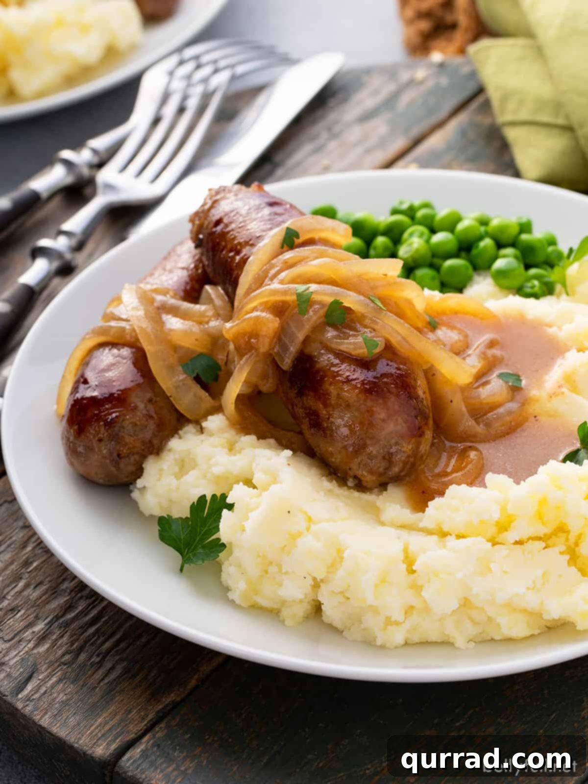 Sizzling Sausages and Creamy Mash 11 Irish pork sausage and rich onion gravy over creamy mashed potatoes, served on a white plate, highlighting the comforting appeal of Bangers and Mash.