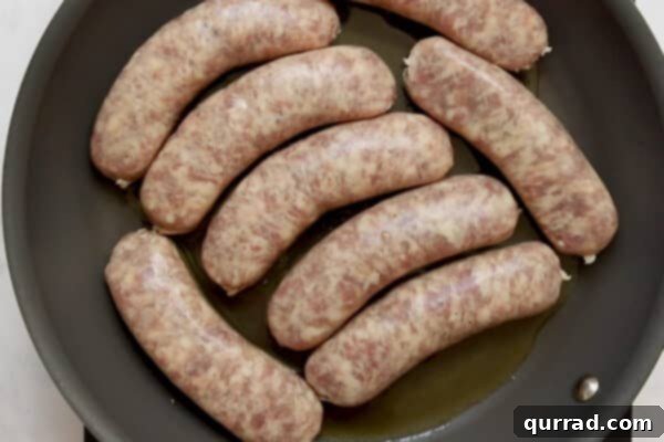 Sizzling Sausages and Creamy Mash 4 Uncooked sausage links arranged neatly in a skillet with olive oil, ready for searing.