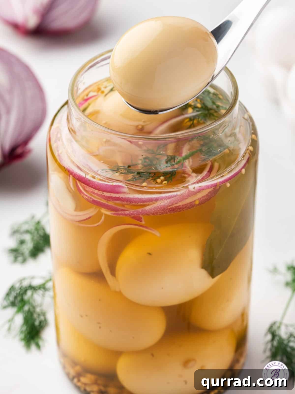 Vinegar-Kissed Eggs 10 Two pickled eggs on a serving spoon held above a glass jar filled with more pickled eggs and brine.