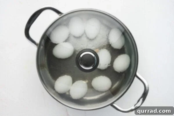 Whole eggs submerged in a pot of boiling water on the stovetop.