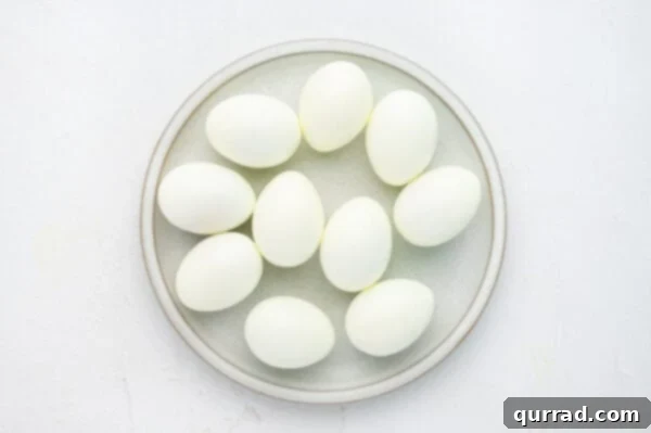 Neatly peeled hard-boiled eggs arranged on a white plate, ready for pickling.