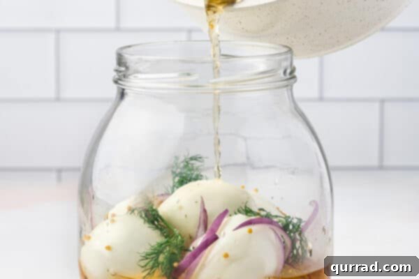 Warm brine being carefully poured over hard-boiled eggs, red onion, and dill in a glass jar.