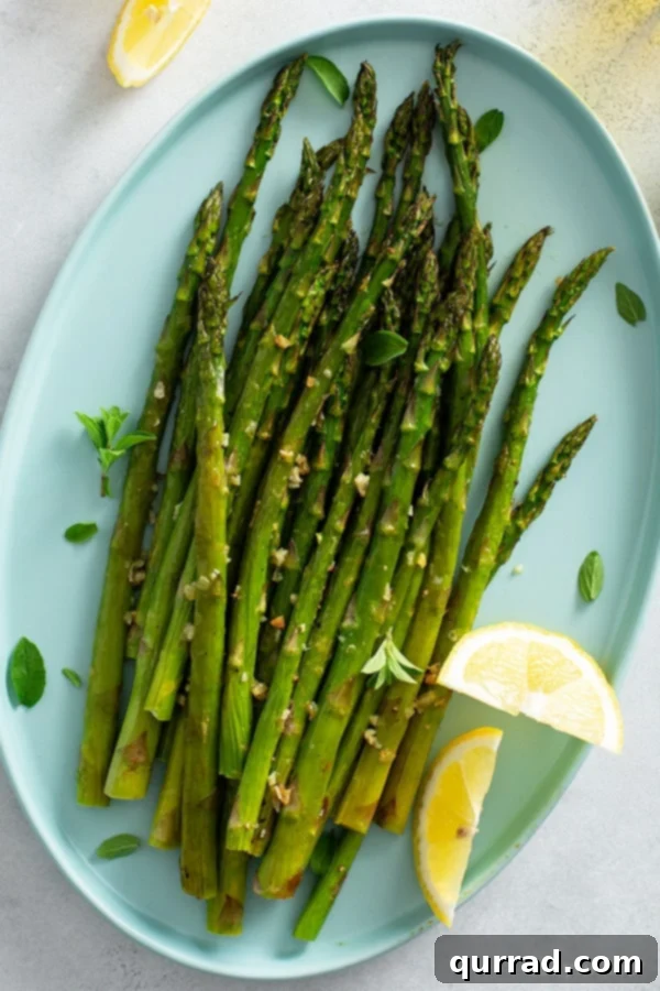 Asparagus, Roasted to Perfection 4 Overhead view of perfectly oven roasted asparagus served on a white plate with fresh lemon wedges, ready to eat.