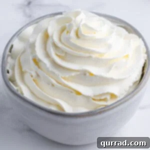 Cloud-Like Homemade Whipped Cream 3 Close-up shot of perfectly swirled homemade whipped cream in a mixing bowl, showcasing its light and airy texture.