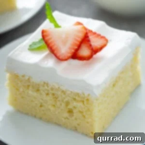 A delicious slice of Tres Leches cake with a bite taken out, garnished with fresh strawberries and mint.