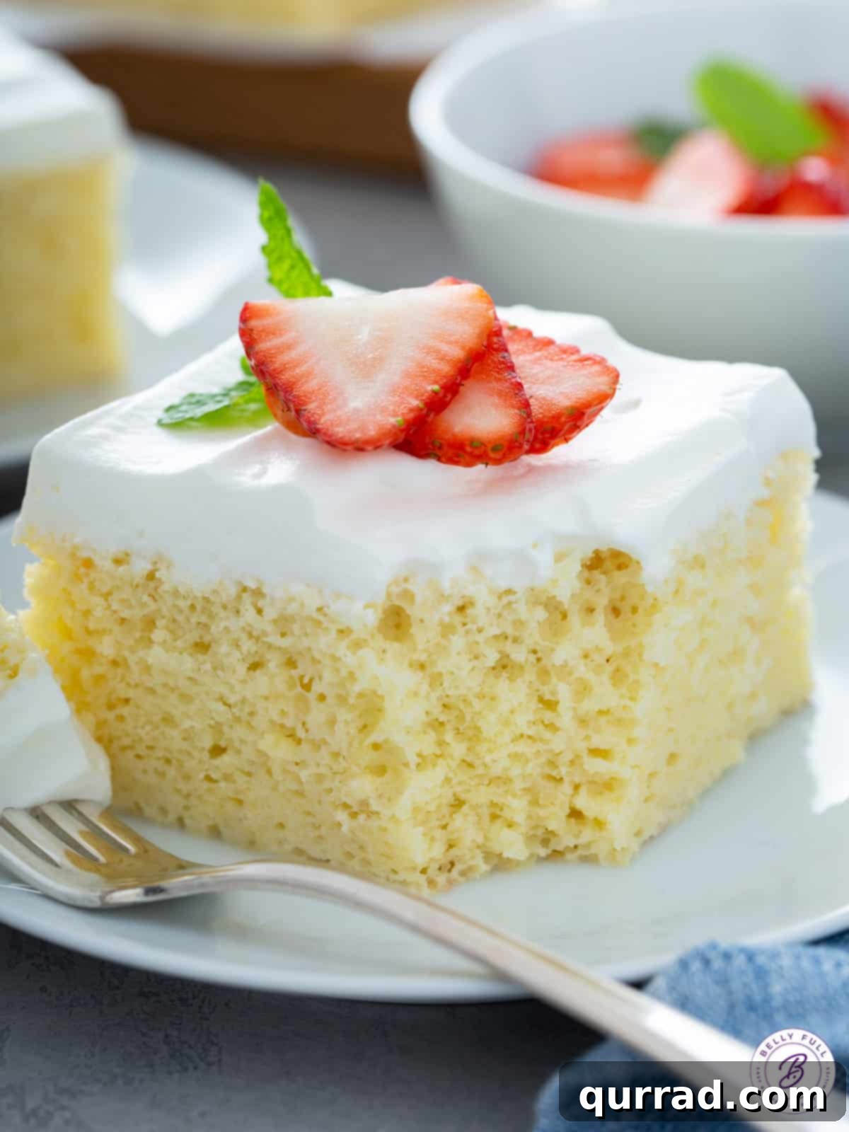 Super Moist Three Milk Cake 5 A close-up of a delightful piece of Tres Leches cake, crowned with sliced strawberries and a tiny bite taken from its corner.