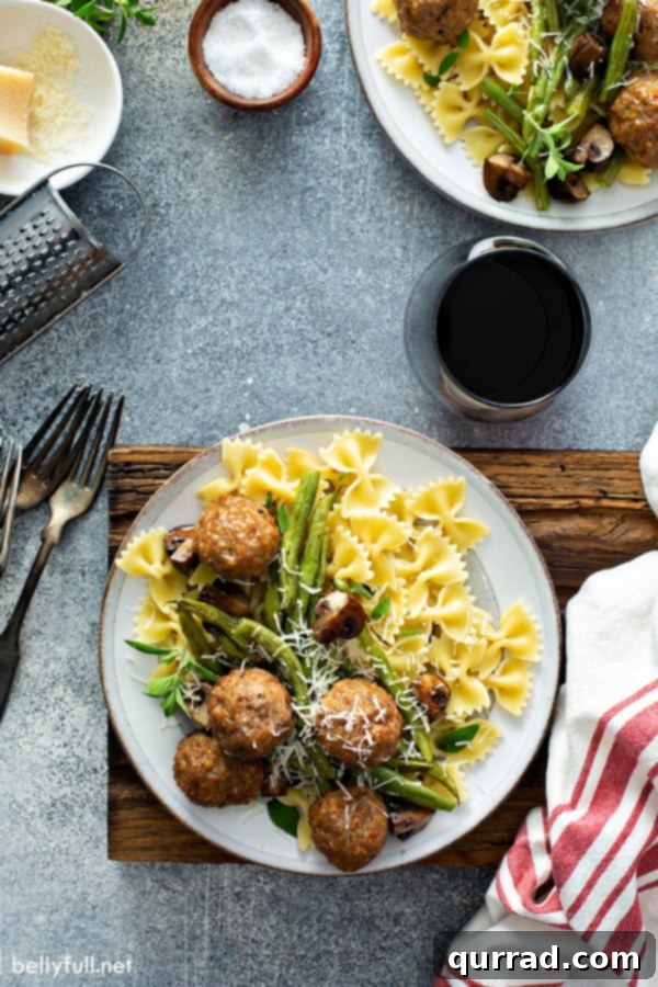 overhead picture of cooked turkey meatballs, green beans, mushrooms, and bowtie pasta on white plate, showcasing a complete sheet pan meal